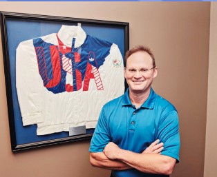 Dr. Curt White standing beside his Olympic weightlifting jacket at White Chiropractic in Mooresville NC